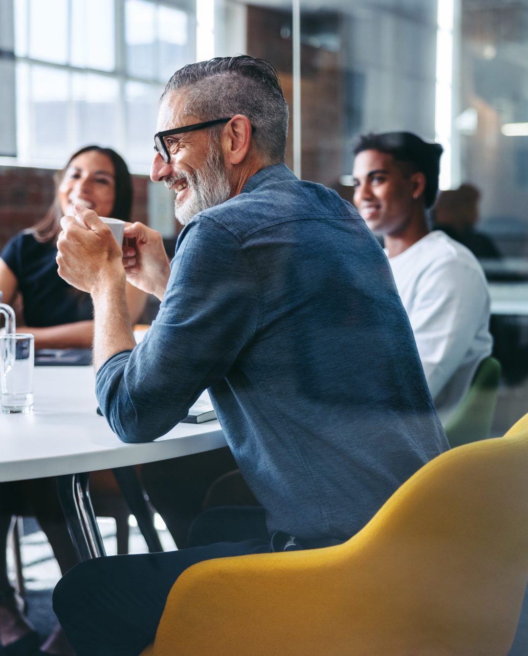 Cheerful mature businessman attending a meeting with his colleagues in an office. Experienced businessman smiling while sitting with his team in a meeting room. Creative businesspeople working together.